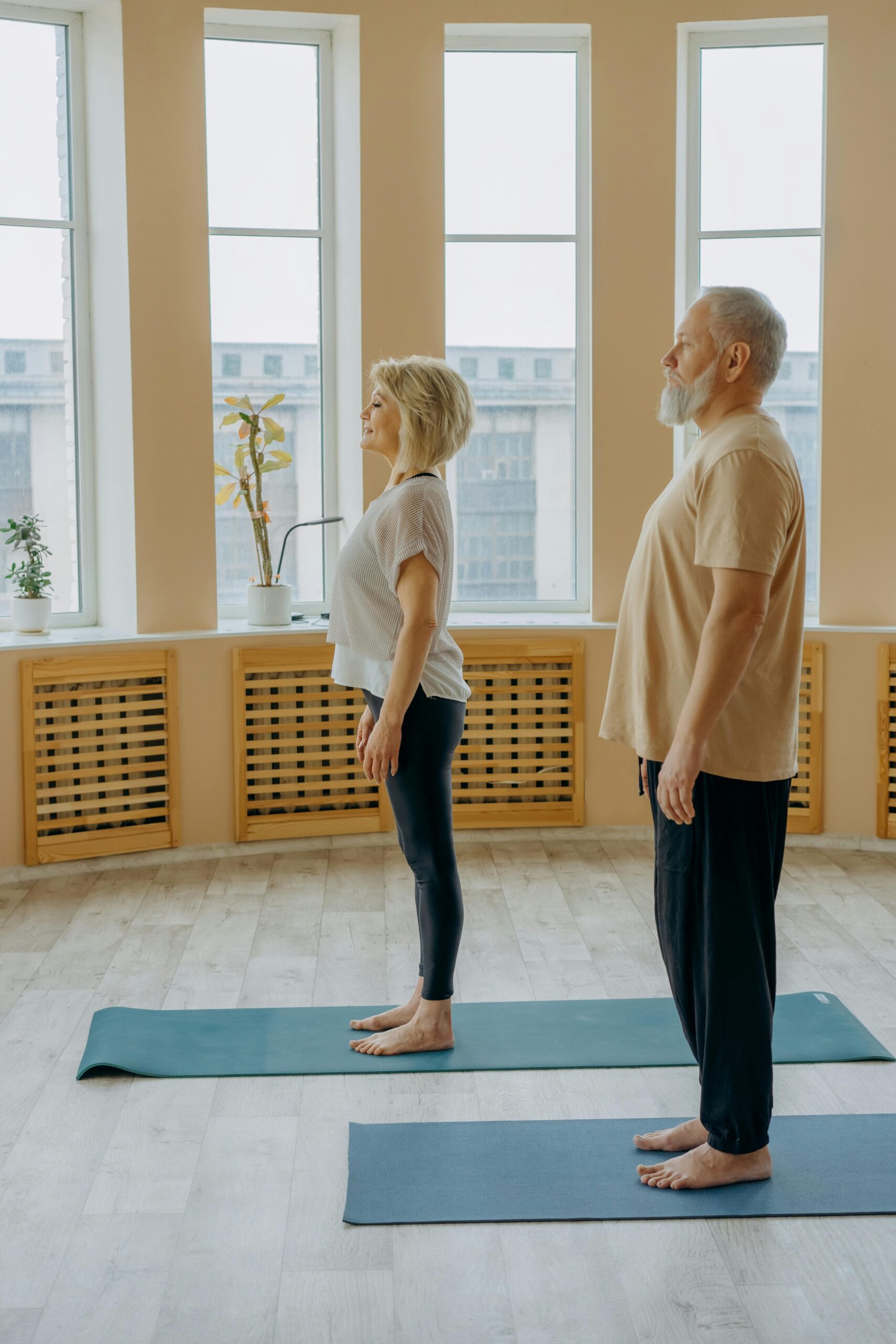 Senior couple standing on yoga mats indoors, focusing on health and fitness.